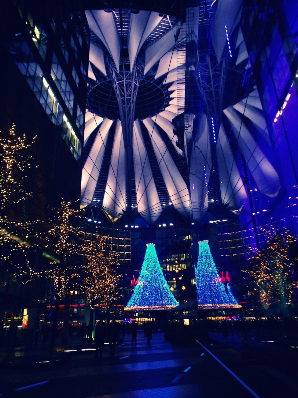 the sony center at potsdamer platz   a tented sky over a plaza built on the widest part of the death strip, two blue cones of light where the watchtowers were. the money came back and lit it like a christmas card. this is the other berlin, the one with a facilities budget.