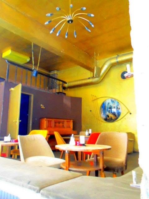 a caf&eacute; furnished out of other people&rsquo;s flats. sputnik lamp, four chairs that don&rsquo;t match, an eye on the wall so you know the room watches back. nobody was designing berlin then. they were just refusing to throw anything out.