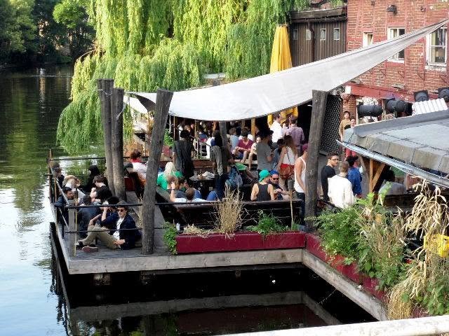 a wooden deck on the flutgraben, full by seven in the evening. that water was the border. everyone is drinking on the death strip and no one mentions it.