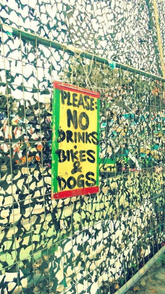 a hand-painted sign wired to camouflage netting: please: no drinks, bikes   dogs. the only rule on the whole lot, and it asked nicely. berlin s authority was one board and a please.