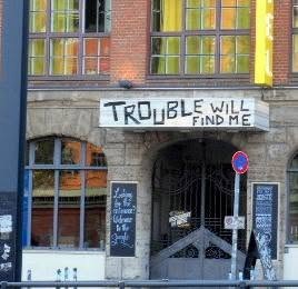 hung over the door, above the chalkboards: TROUBLE WILL FIND ME. a whole city&rsquo;s fatalism used as a welcome mat. not keep out &mdash; just, it&rsquo;s coming anyway. come in.