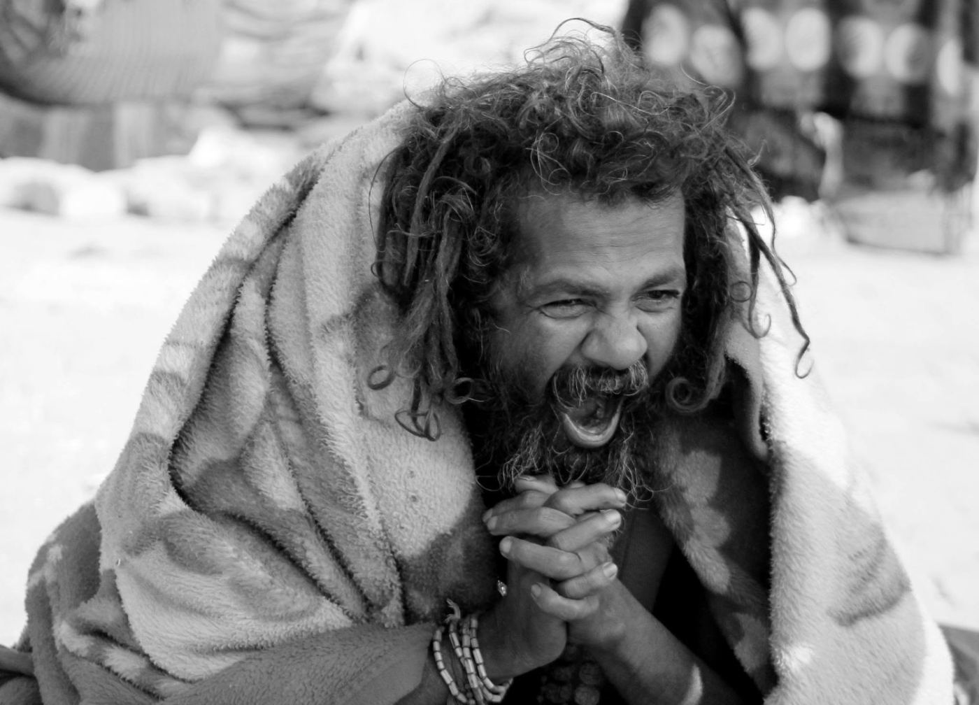 a sadhu wrapped in a blanket, laughing, shot in black and white