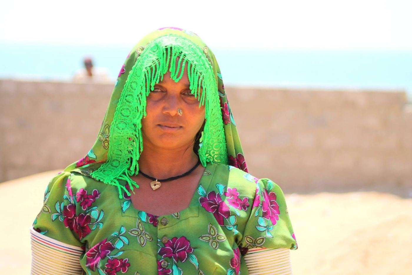 a green veil on a rooftop, the sea behind her.