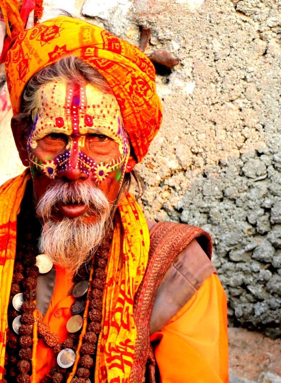 a sadhu in saffron, face painted, coins and rudraksha round his neck