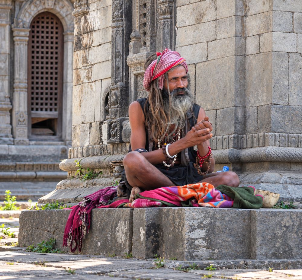 A sadhu seated cross-legged on a plinth, counting rudraksha beads