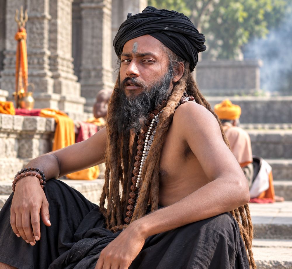 A young sadhu in black turban and long dreadlocks, smoke rising behind