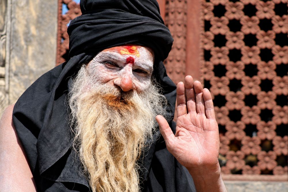 A black-clad, ash-faced sadhu raising his right palm