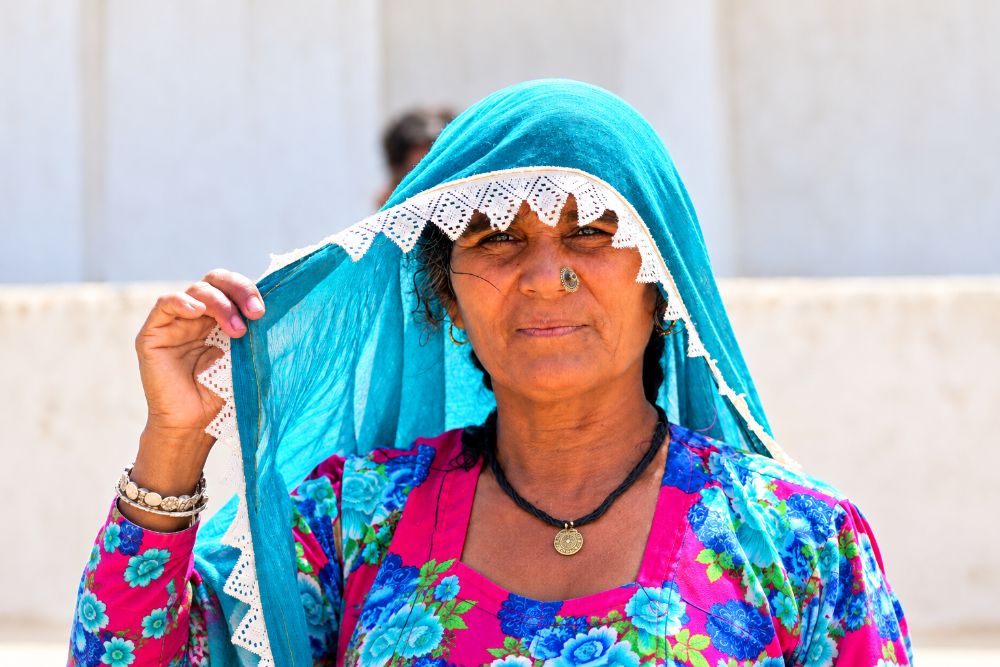 A woman holding a teal lace-edged dupatta over her head like a canopy