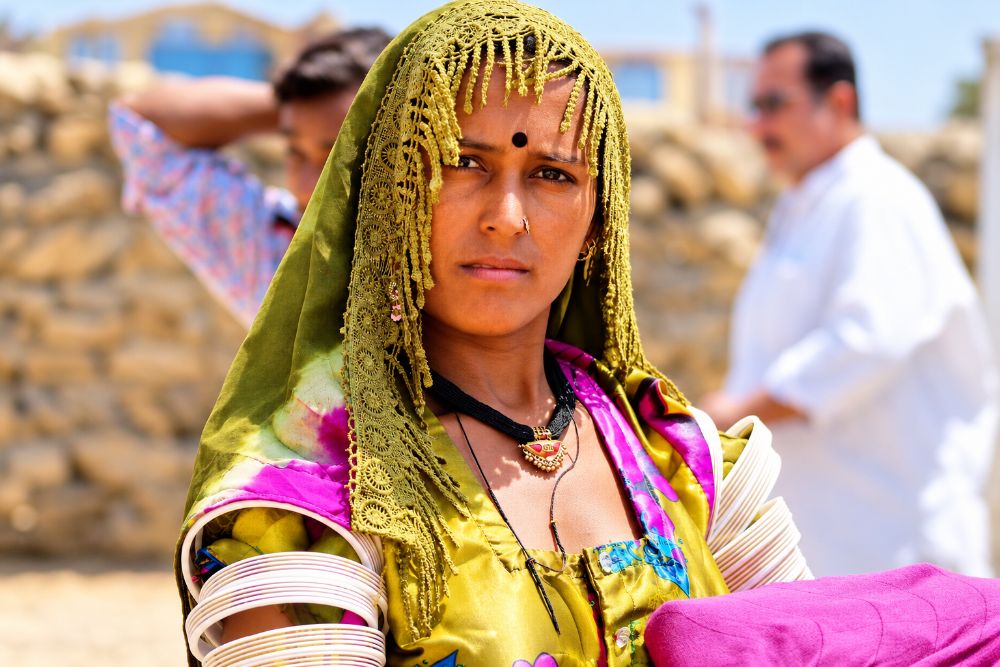 A young woman in an olive lace veil, black bindi, nose ring, white bangles up the arm