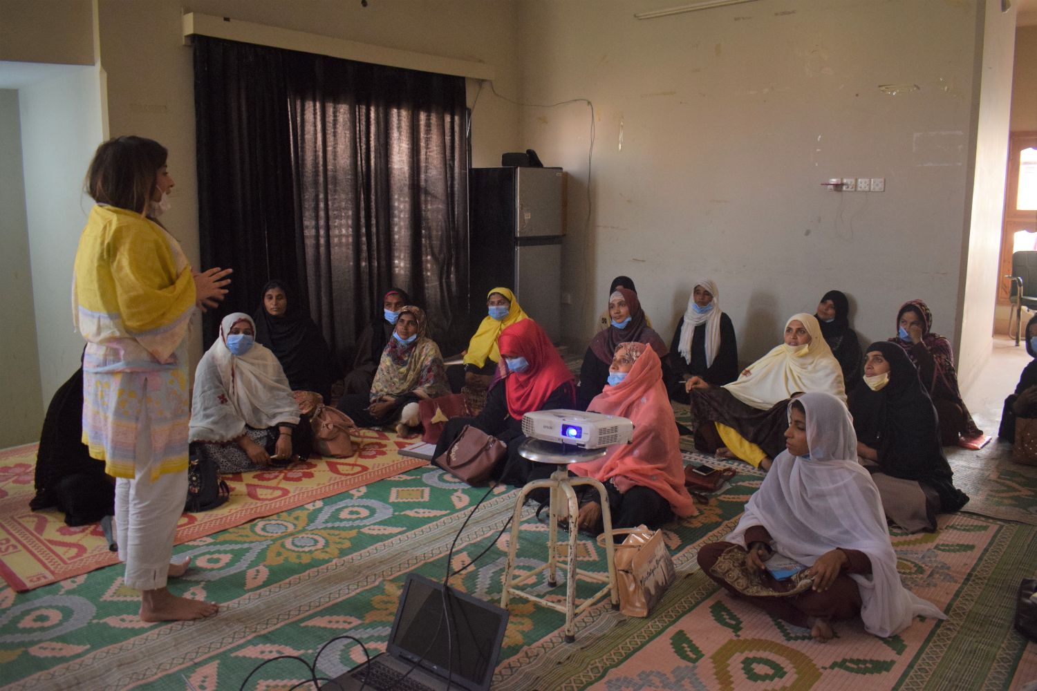 Saba presenting barefoot to women seated on floor mats