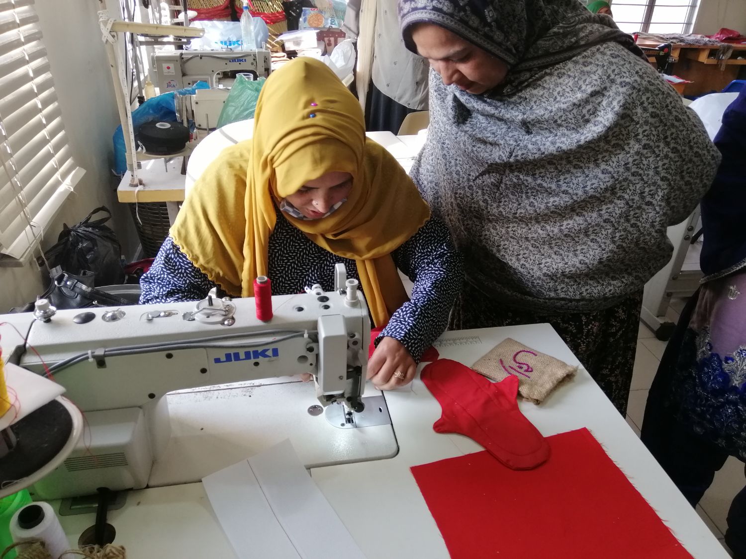 Meera stitches a pad on a Juki machine as a trainee watches