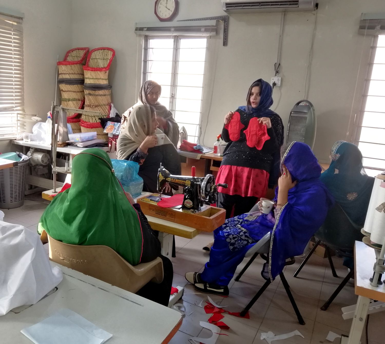 A training room of women in bright headscarves at sewing machines