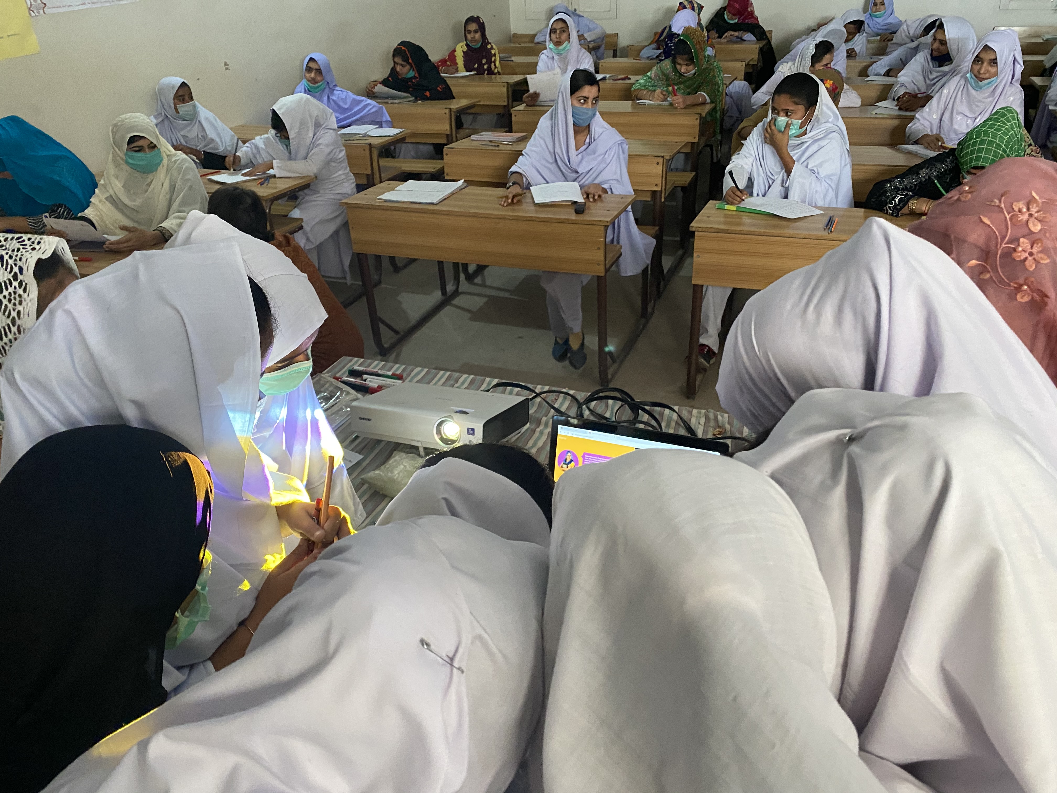 Students crowd around a laptop with a projector light on their faces