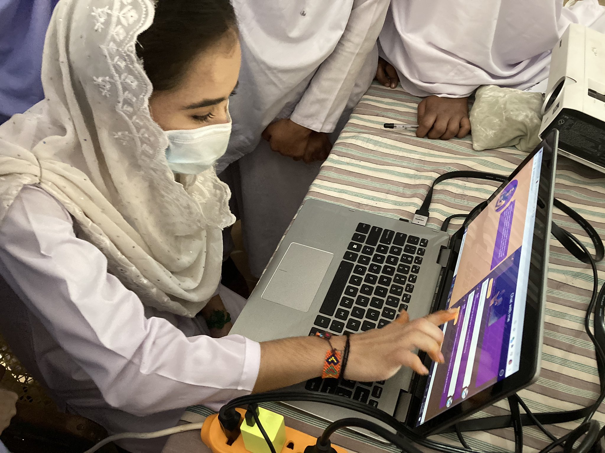 A masked young woman points at Raaji on a laptop screen