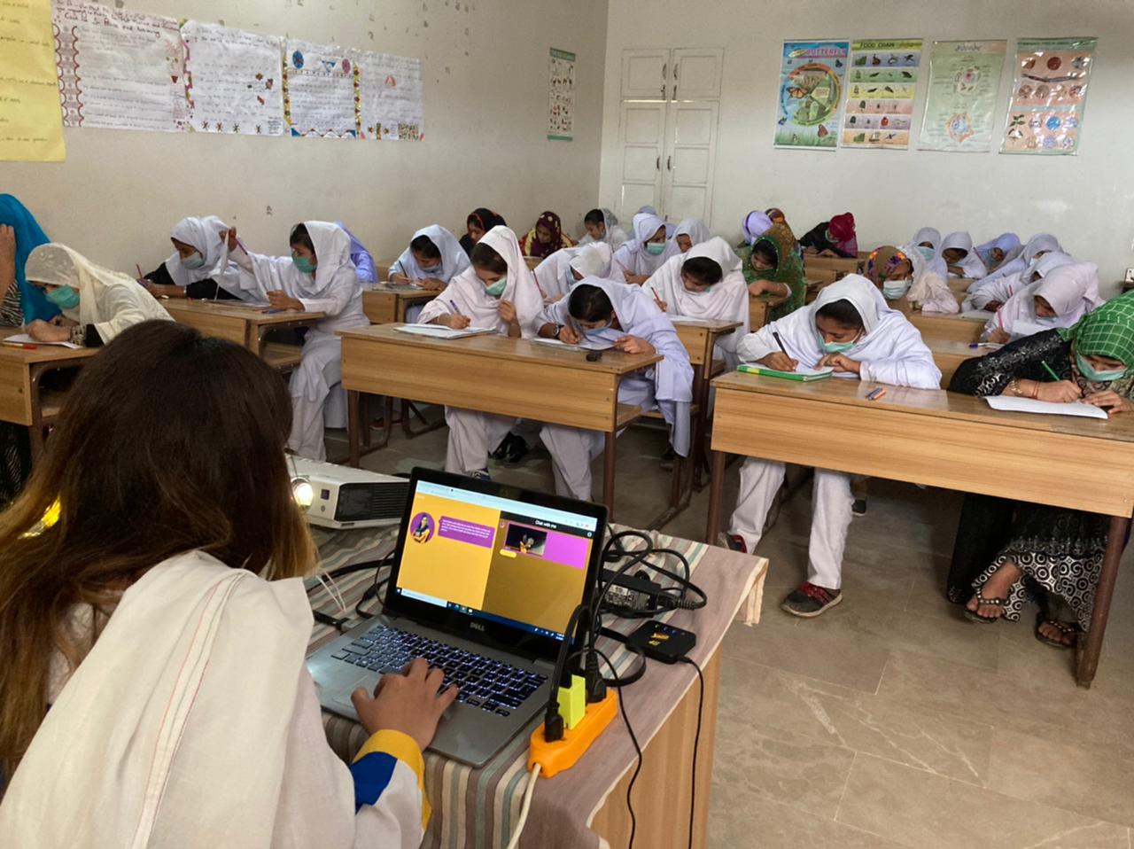 A classroom of girls writing while Raaji runs