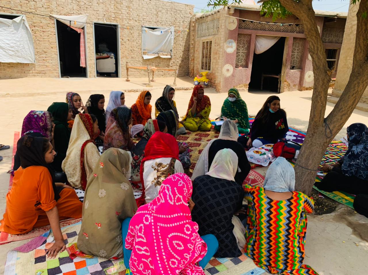 Girls in a circle under a tree in a village courtyard