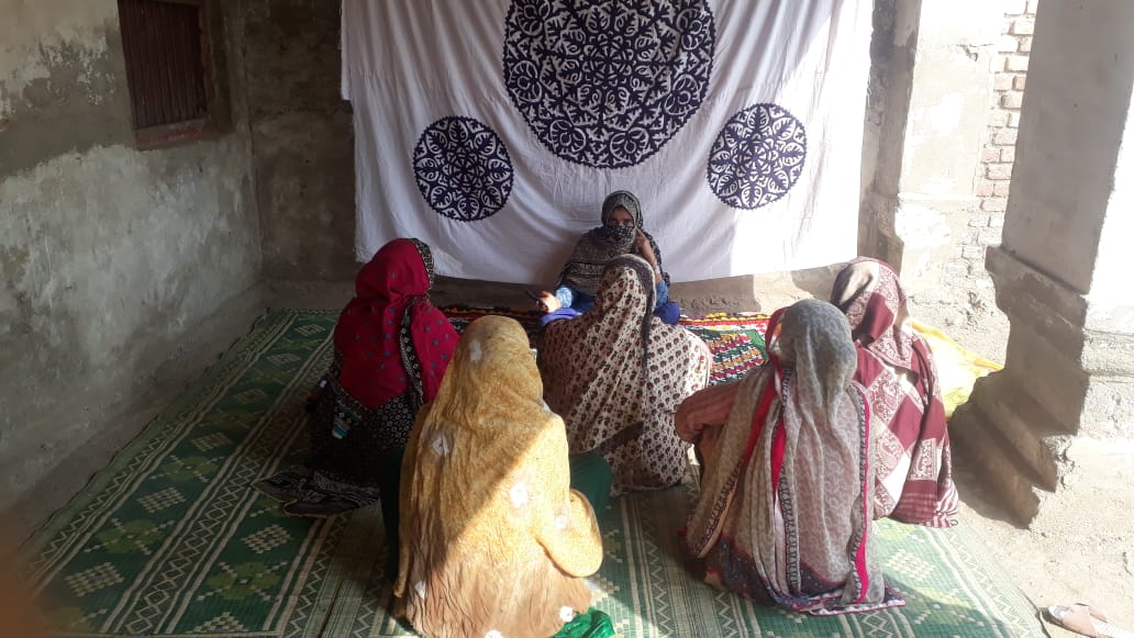 Women seated before a blue and white embroidered rilli