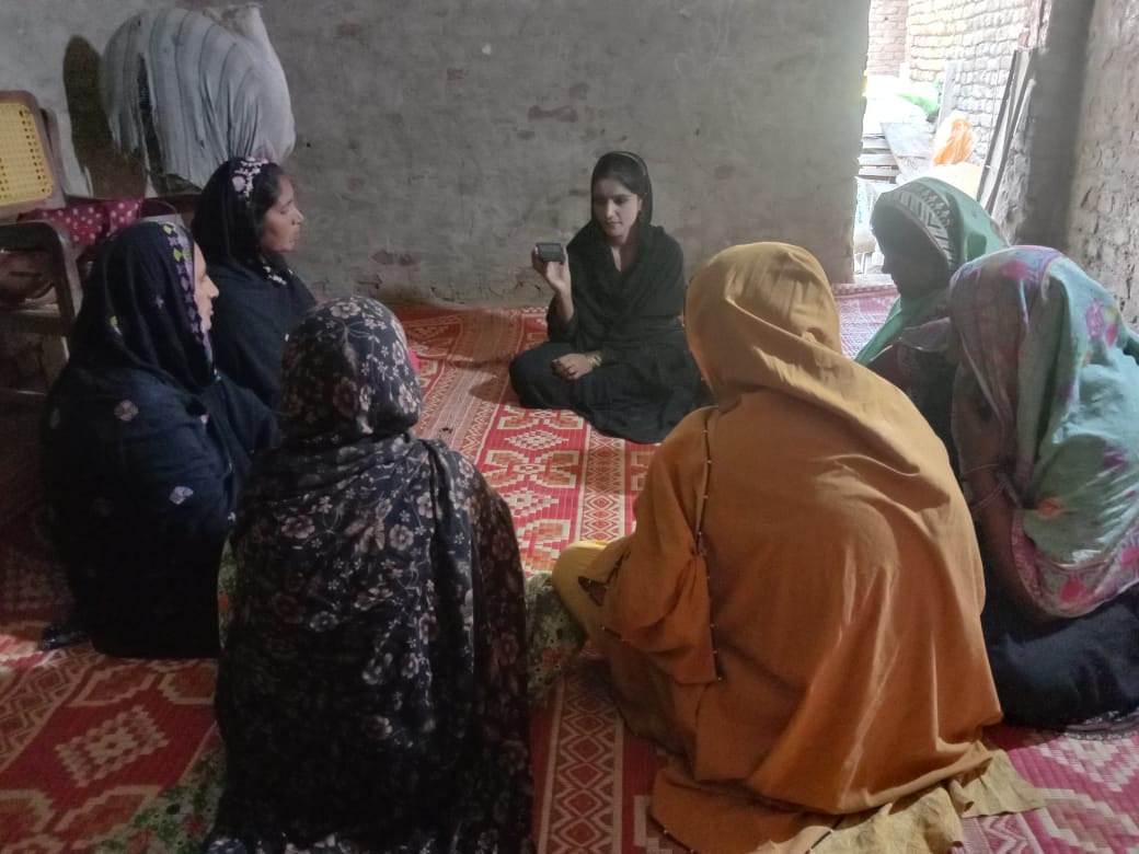 Women in a circle in a brick courtyard, one holding a phone