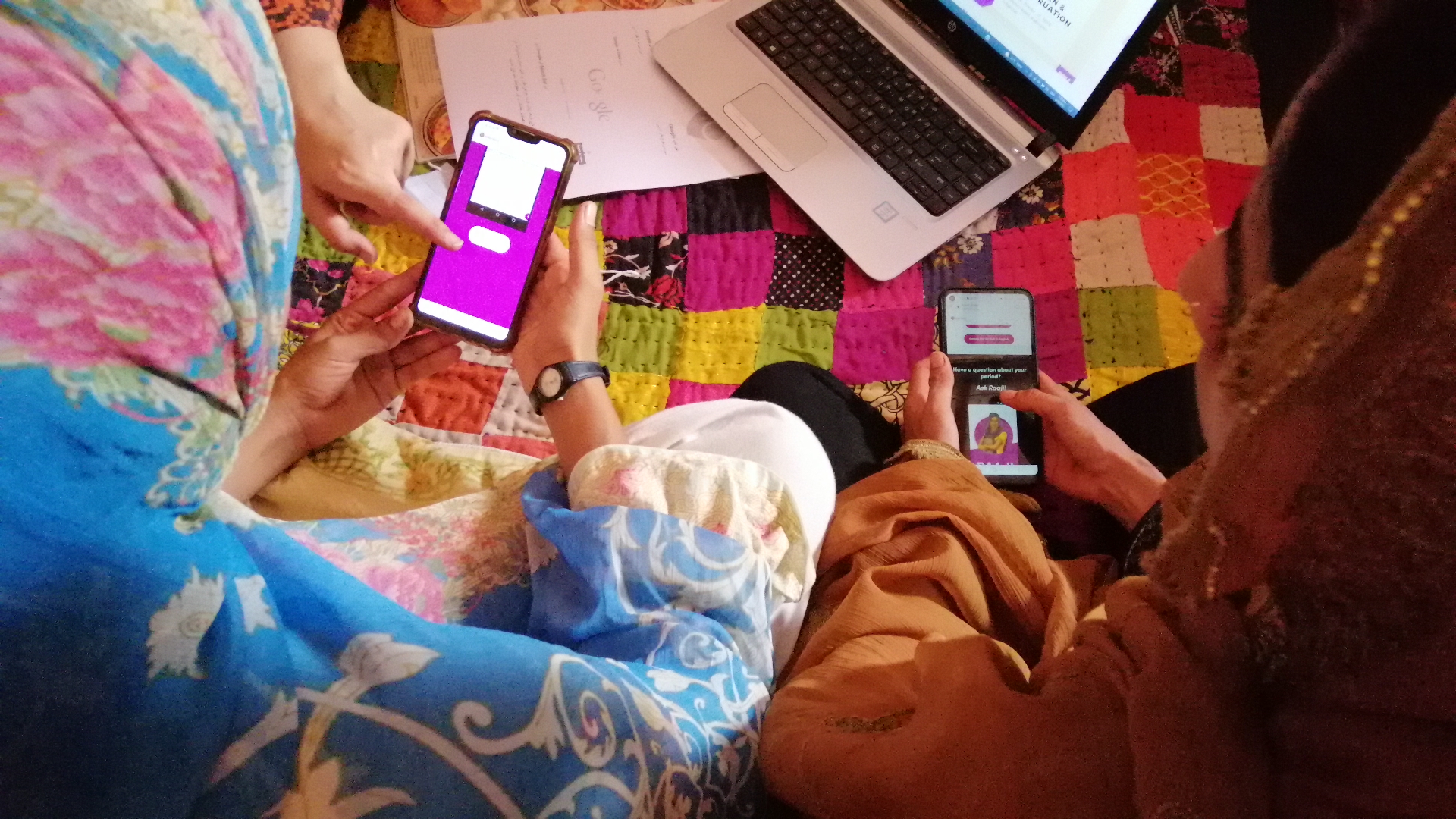 Two phones running Raaji held in women's hands over a quilt