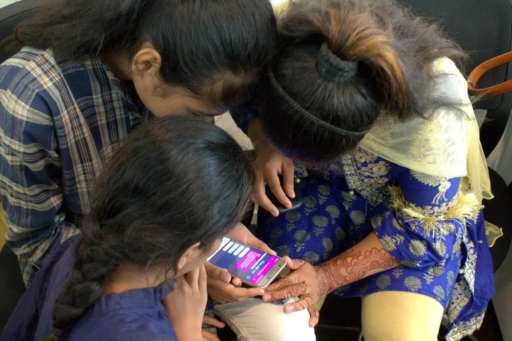 Three girls huddled over a phone running Raaji