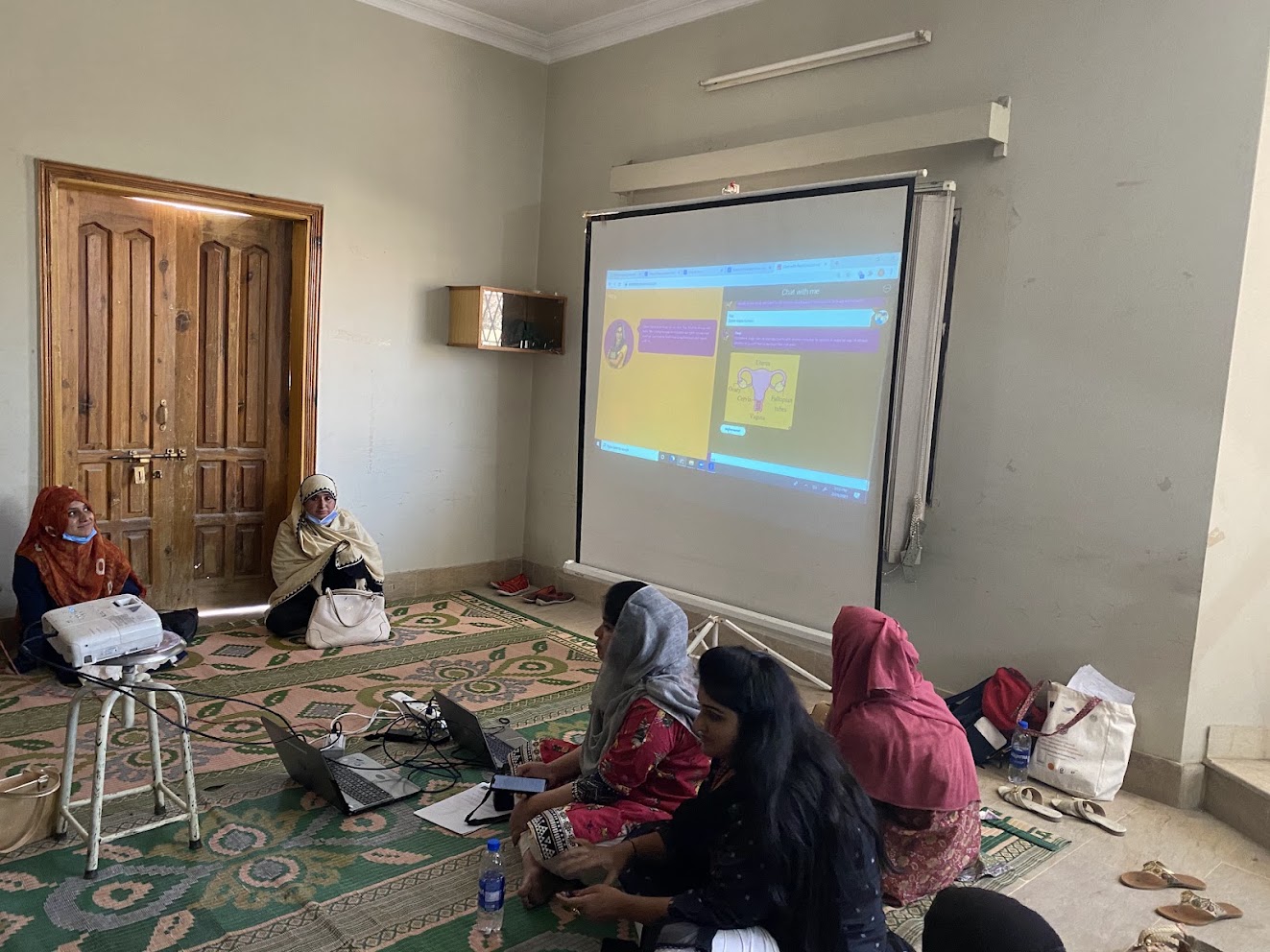 Raaji projected in a small room with women on the floor